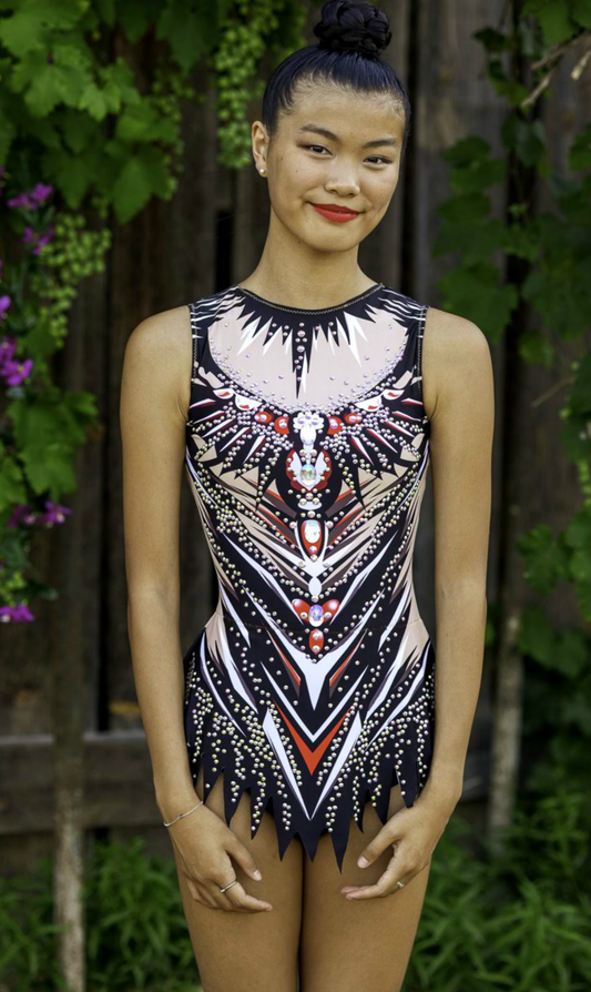 Maillot deportivo impactante con diseño tribal en tonos negro, rojo y nude, decorado con pedrería brillante. Corte cómodo y tejido elástico que se adapta al cuerpo, ideal para competencias de gimnasia, danza o patinaje.